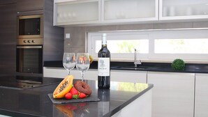 A modern kitchen with a built-in oven, a wine bottle, and fresh fruits on the counter. - Luxury Villa w/ Jacuzzi and Heatable Pool (Armação de Pêra)