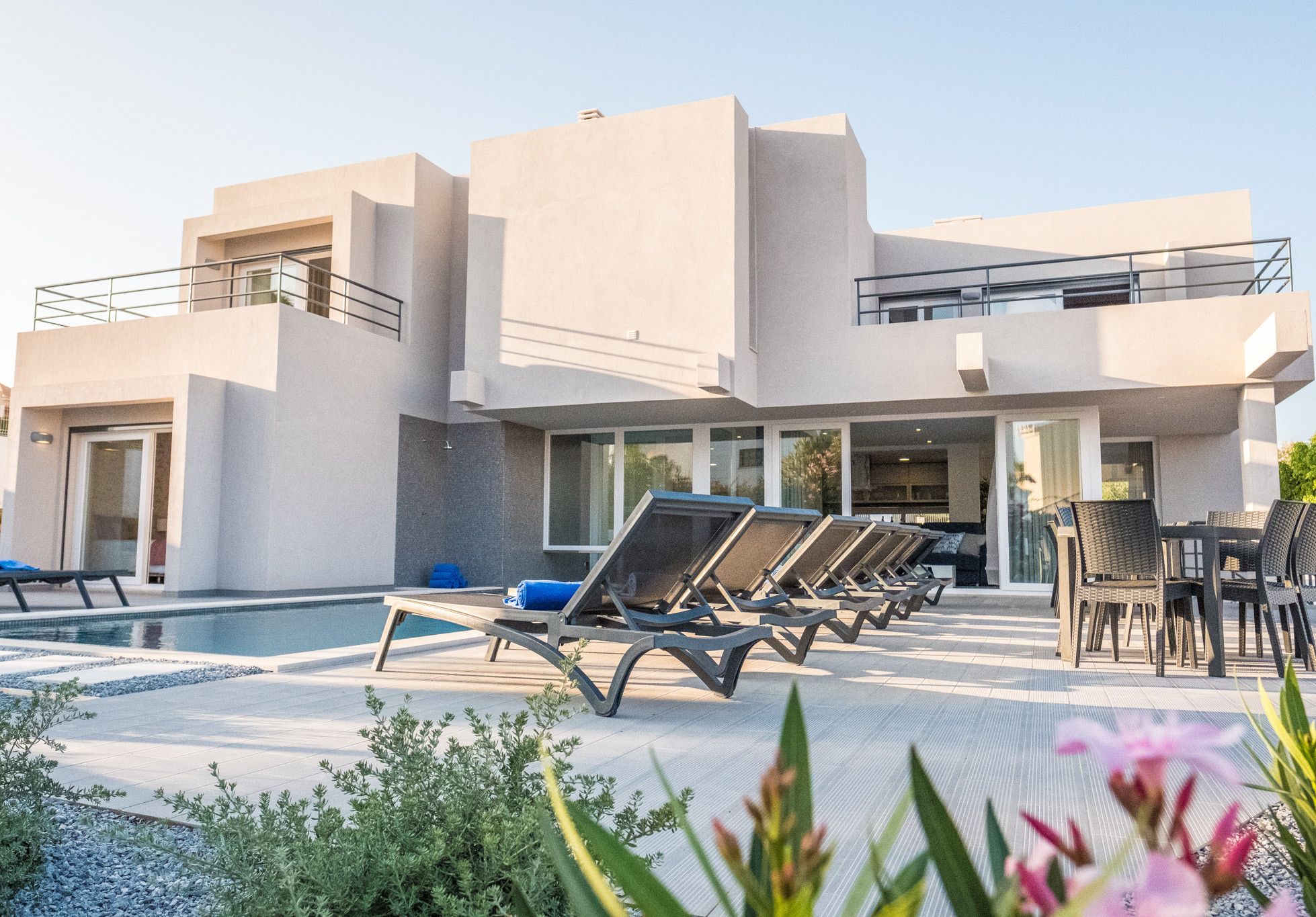 A modern building with a pool area, including lounge chairs and a dining table.