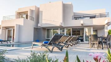 A modern building with a pool area, including lounge chairs and a dining table.