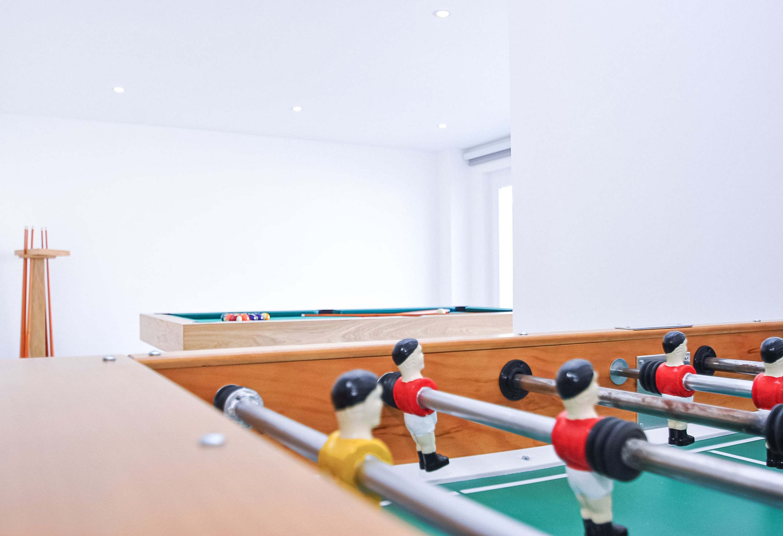 A foosball table in a room with a pool table and a wooden cabinet.