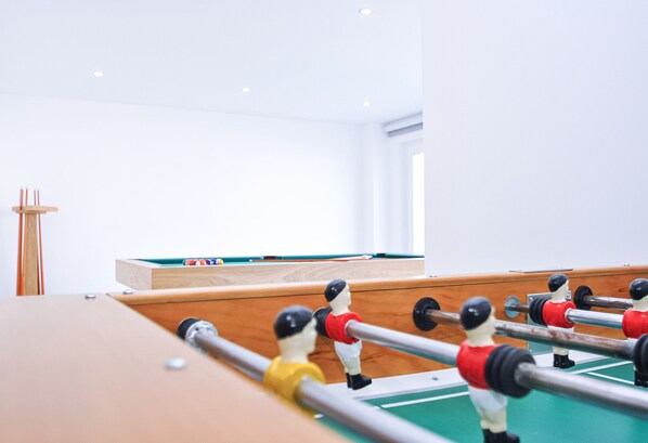 A foosball table in a room with a pool table and a wooden cabinet.