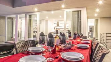 A dining area with a long table set for a meal, including plates, glasses, and a bottle of wine.