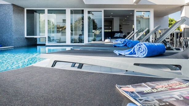 A modern pool area with lounge chairs and towels, a magazine on a chair, and a clear view of the pool. - Luxury Villa w/ Jacuzzi and Heatable Pool (Armação de Pêra)