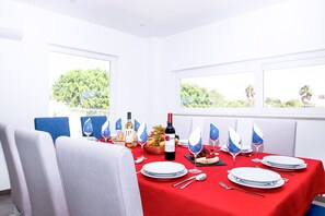A dining area with a red tablecloth, white plates, and blue napkins. There is a bottle of wine and a basket of fruit on the table. - Luxury Villa w/ Jacuzzi and Heatable Pool (Armação de Pêra)
