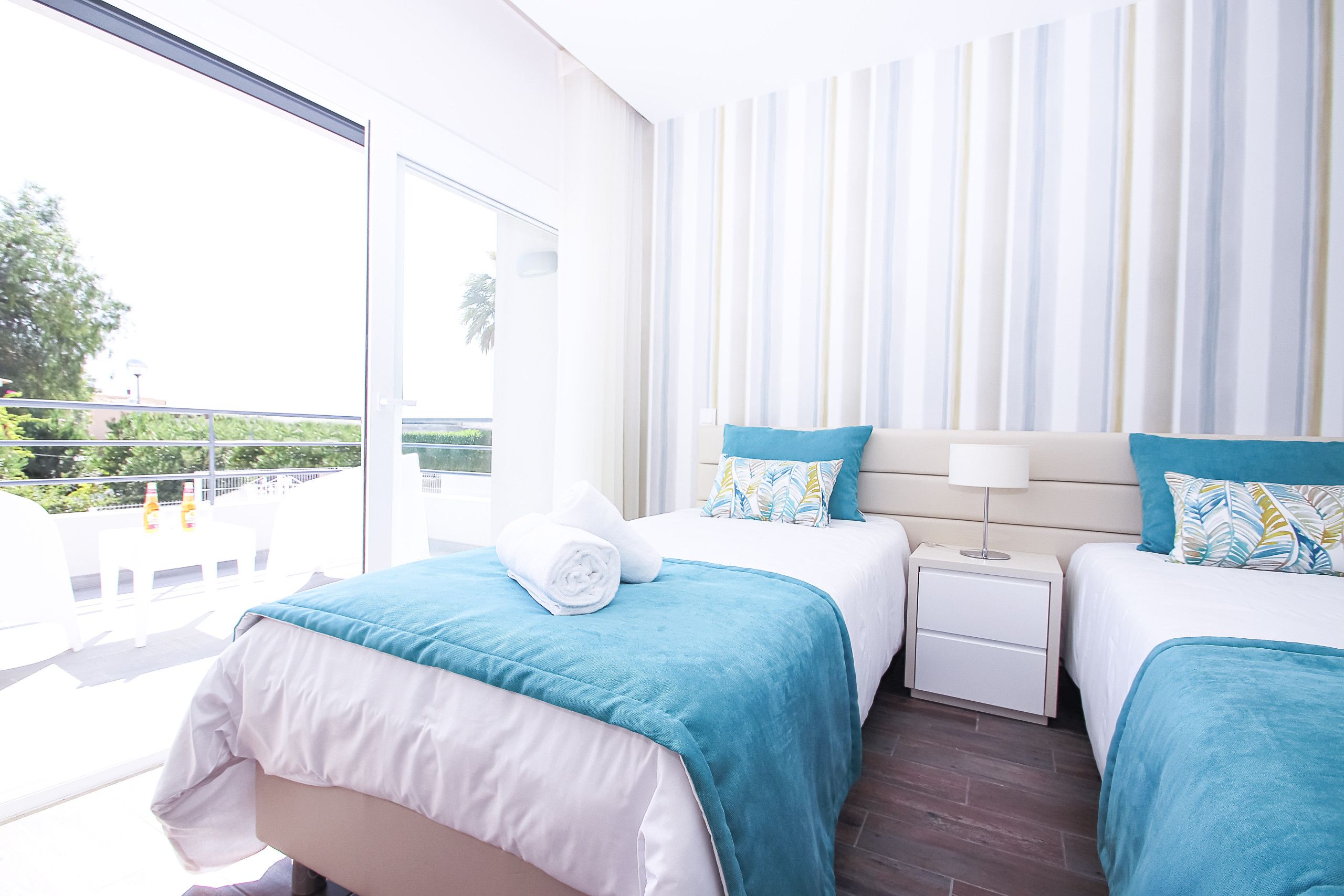 A hotel room with two beds, a balcony, and a view of greenery.