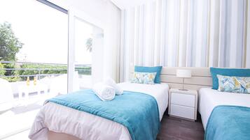 A hotel room with two beds, a balcony, and a view of greenery.