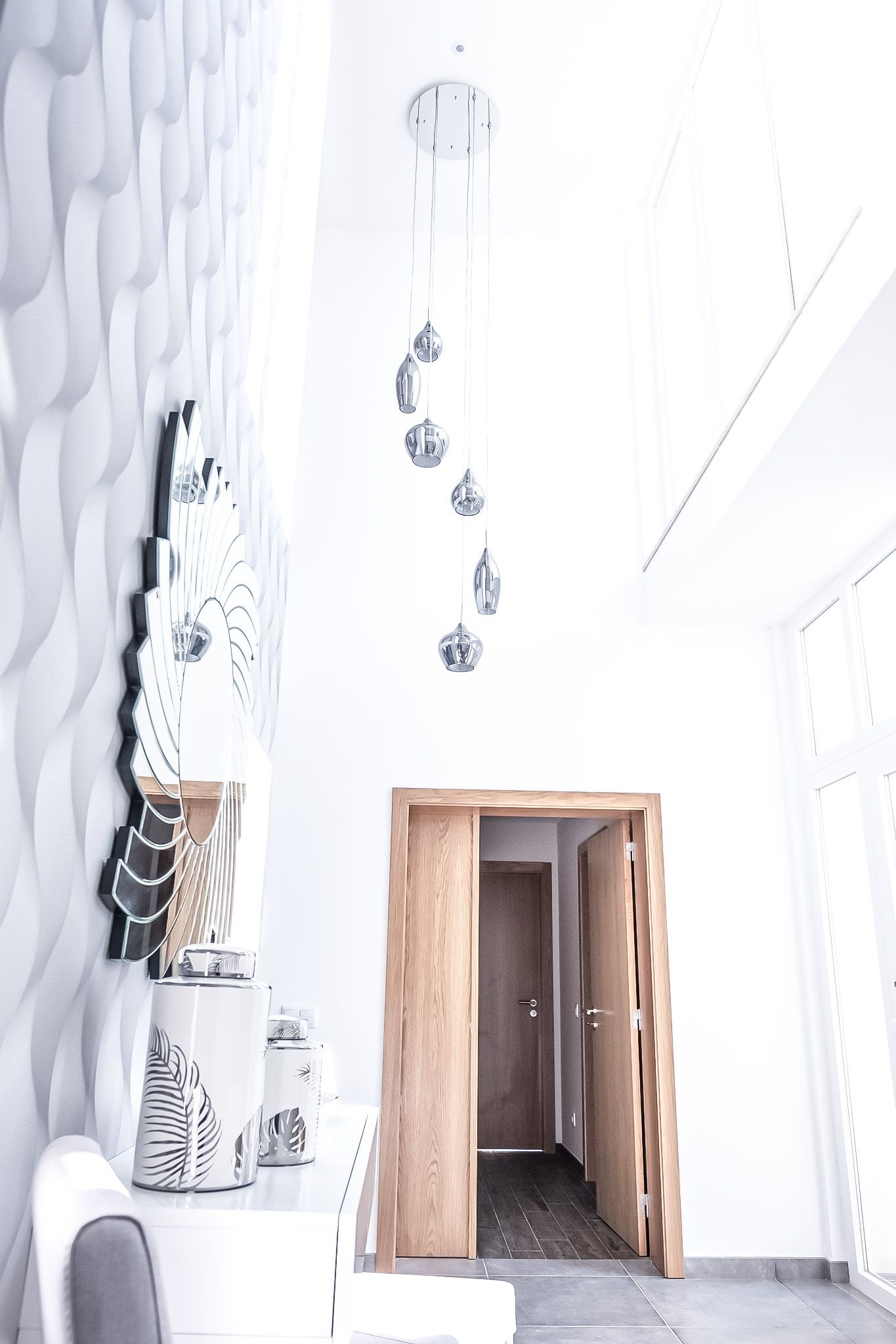 A modern interior with a white textured wall, a wooden door leading to a hallway, and a hanging light fixture.