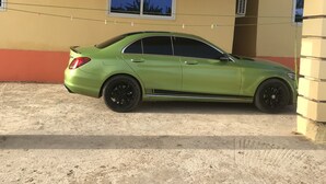 Une voiture verte est garée devant un immeuble à la façade jaune et rouge, avec une fenêtre et un petit climatiseur.