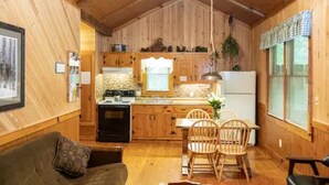 Ein gemütliches Blockhaus-Interieur mit Holzvertäfelung, einer Essecke mit Stühlen, einer Küche mit Holdeinrichtungen und einem Deckenventilator.