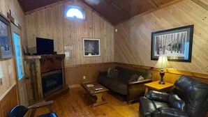 Ein gemütliches Holz-Interieur mit Deckenventilator, Kamin, Sofa, Couchtisch und einem gerahmten Bild an der Wand.