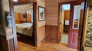 Ein Holzinnenraum mit einem Bett, einer Tür zu einem Badezimmer und einem Feuerlöscher auf einem Regal.