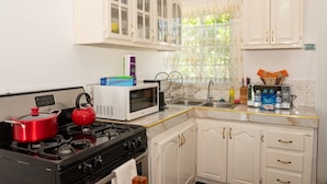 Una cocina con armarios blancos, microondas, estufa a gas y hervidor.