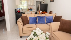 Una sala de estar con un sofá color beige, una mesa de comedor y una cocina al fondo.