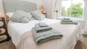 Una cama bien hecha con un cabecero estampado, una lámpara de noche y una ventana con cortinas.