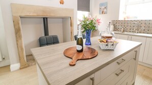 Una cocina moderna con una isla de madera, una botella de vino, un florero con flores y una cesta de pan.