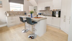 Una cocina moderna con armarios blancos, una isla central con taburetes de bar, un salpicadero decorativo y un amplio ventanal.