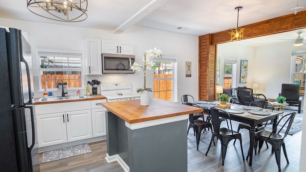 A modern kitchen with white cabinets, a central island, and a dining area with black chairs.
