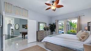 A bedroom with a bed, a ceiling fan, a dresser, a mirror, and a view of the outdoors. - Palm Coast Oasis Retreat- 15 min to beach (Palm Coast)