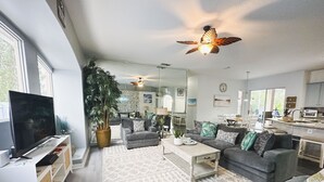 A modern living room with a large flat-screen TV, grey sofas, a coffee table, and a ceiling fan. - Palm Coast Oasis Retreat- 15 min to beach (Palm Coast)