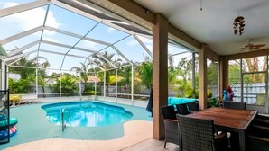 A covered outdoor swimming pool with a glass ceiling, surrounded by wicker furniture and a wooden table. - Palm Coast Oasis Retreat- 15 min to beach (Palm Coast)