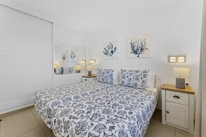 A bedroom with a bed, bedside tables, wall-mounted lamps, and artwork.