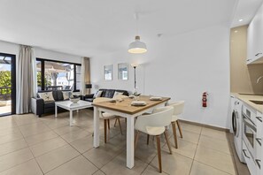 A modern living room with a dining table, sofa, and chairs, a kitchen area, and a large window with curtains.