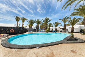 A swimming pool with lounge chairs, palm trees, and white buildings. - Casahost Bastian Boutique II Seaview (Costa Teguise)
