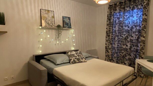 A compact bedroom with a bed, bedside tables, a desk, and a ceiling light fixture.