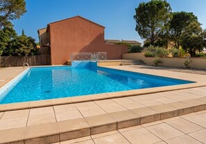 A rectangular swimming pool with a metal ladder, surrounded by a tiled deck.