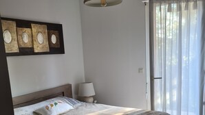 Una camera da letto con un letto, un comodino, una lampada e una finestra con tende leggere.