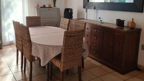 Un'area pranzo con un tavolo rotondo, sedie in vimini, un mobile e un grande specchio a parete.