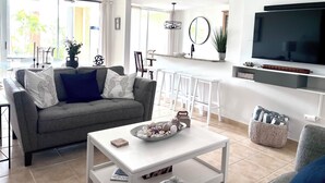 Een moderne woonkamer met een grijze bank, een witte salontafel en een aan de muur bevestigde televisie.