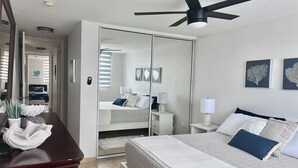 Een slaapkamer met een bed, nachtkastjes, een plafondventilator, een kledingkast en een spiegel.