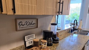 Een keuken met houten kasten, een granieten aanrecht, een koffiezetapparaat en een bordje met de tekst 'Onze keuken. Als ik het moest roeren, is het zelfgemaakt'.