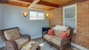 A cozy room with wicker furniture, a brick wall, and a ceiling with wooden beams. - Walk to Lake Erie: Chic Home, Private Yard & Deck (Avon Lake)