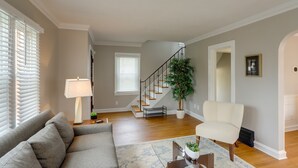 A living room with a gray sofa, a white armchair, a coffee table, and a staircase leading to another level. - Walk to Lake Erie: Chic Home, Private Yard & Deck (Avon Lake)