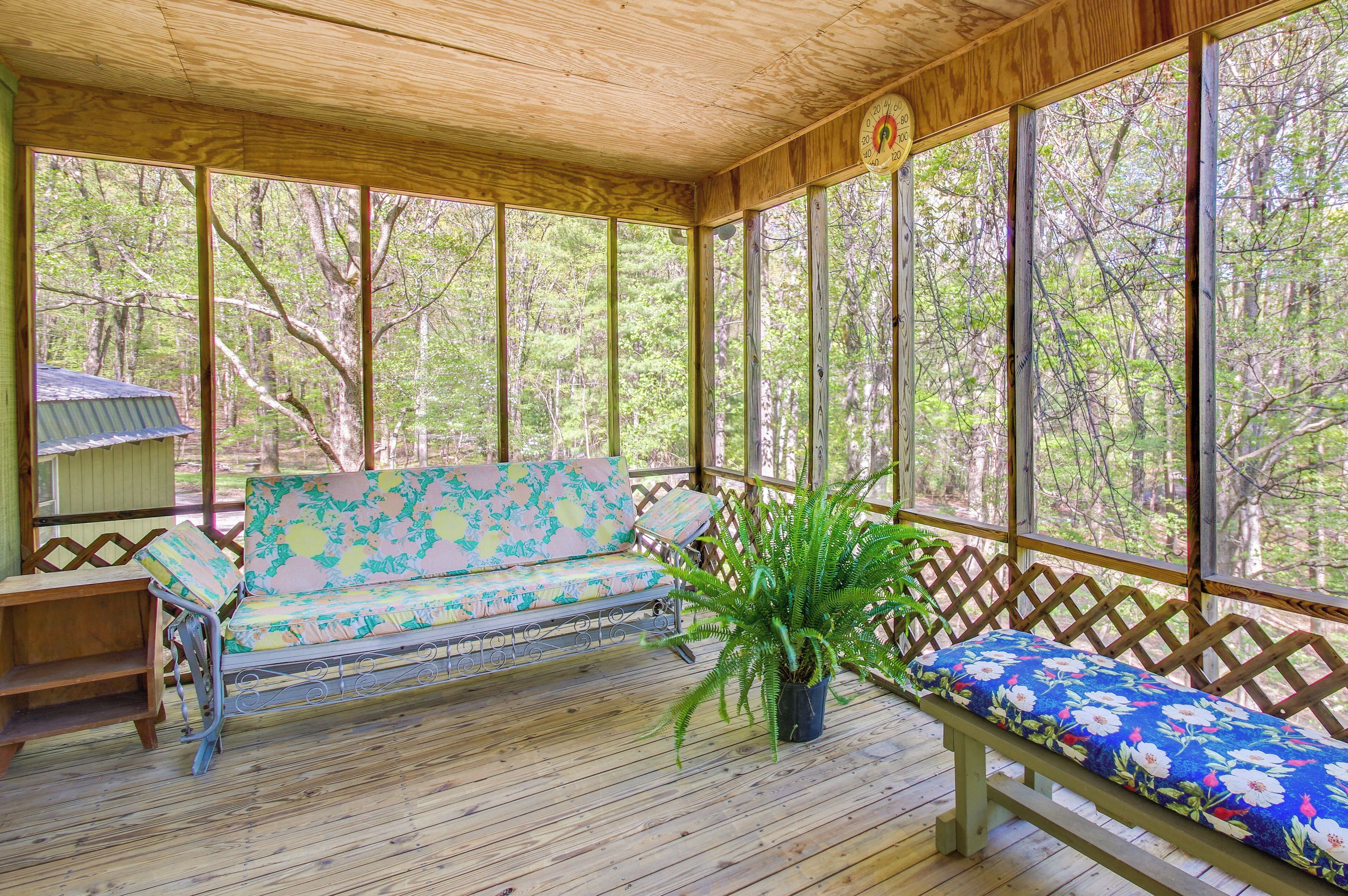 A covered porch with a wooden bench, a cushioned bench with a floral cushion, and a potted plant.