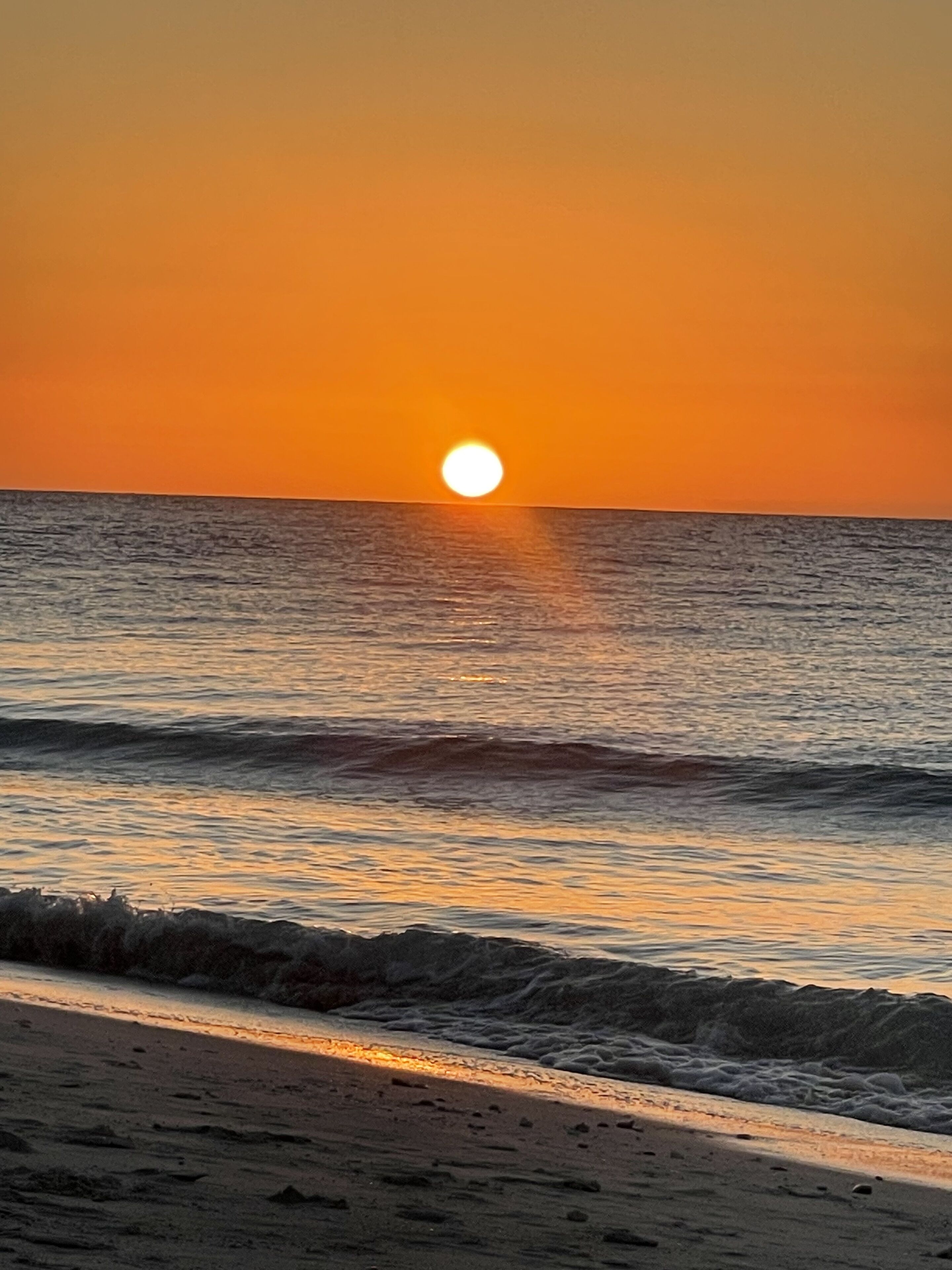 Un atardecer sobre una playa con olas acercándose a la orilla.