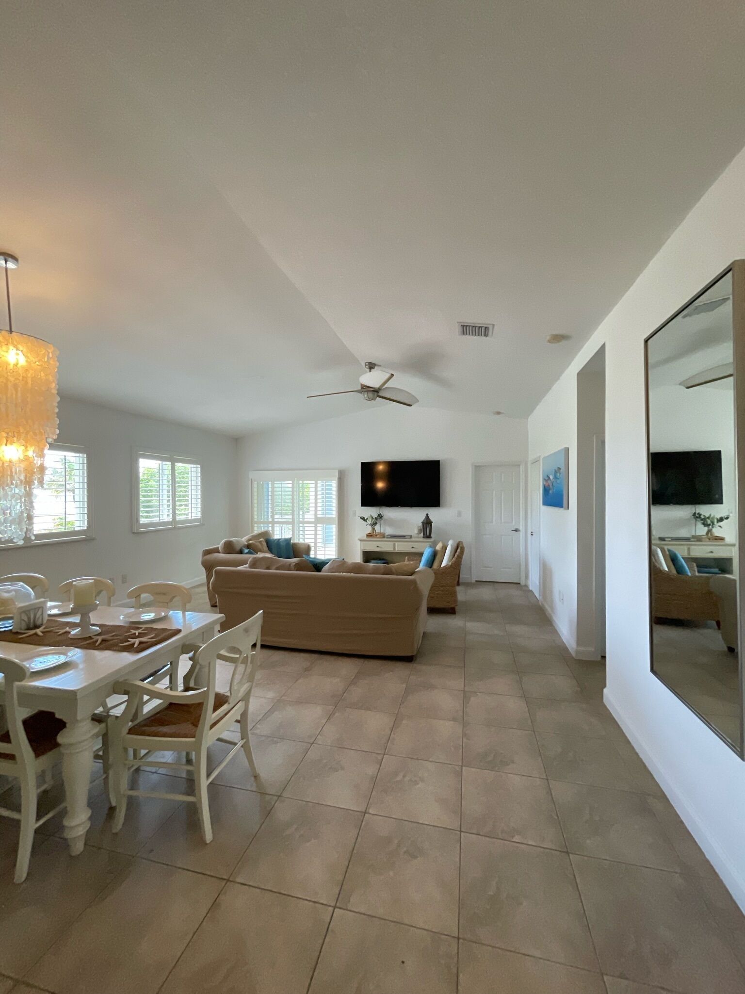 A spacious living area with a dining table, chairs, sofas, and a ceiling fan.