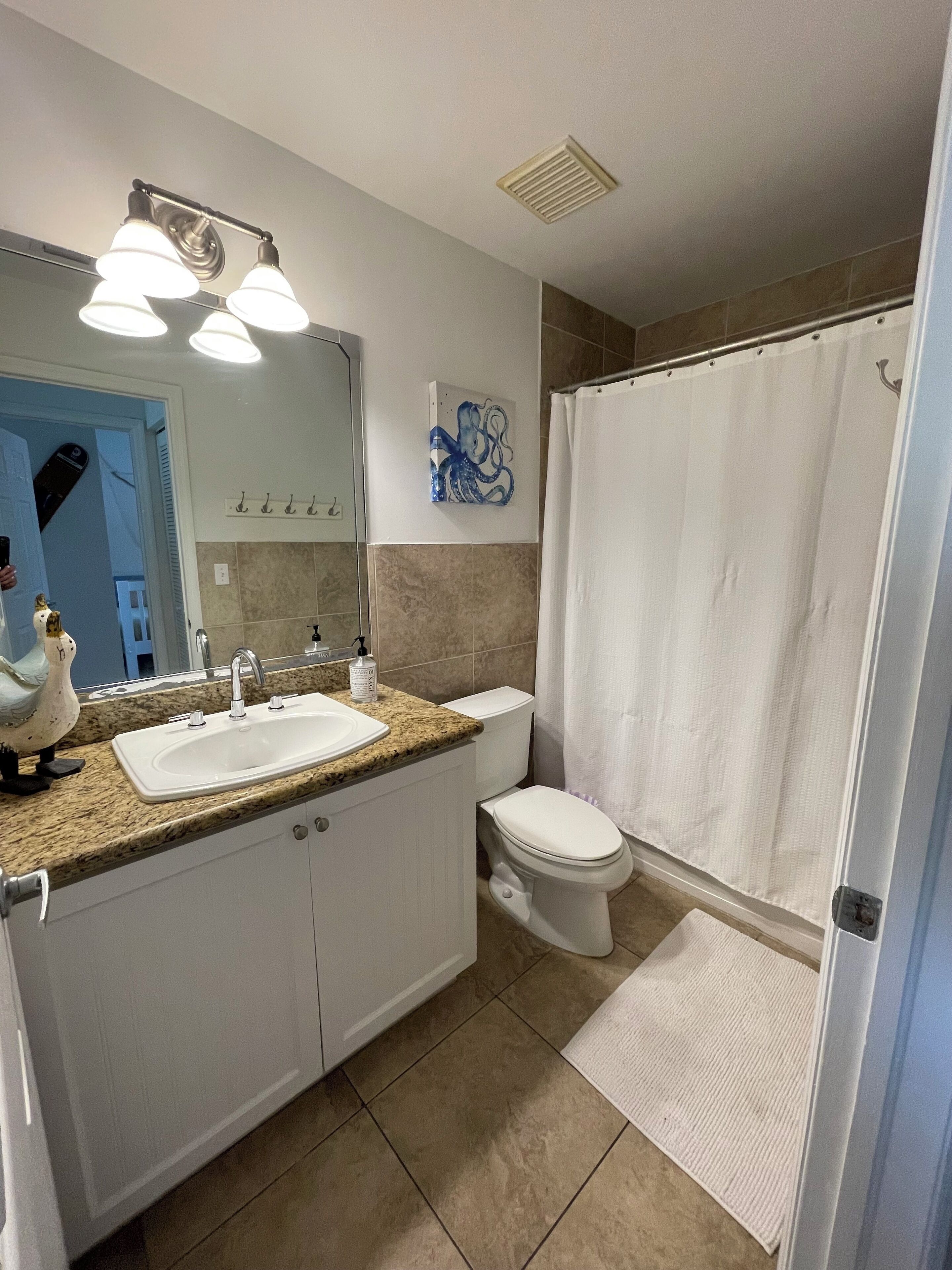 A bathroom with a double sink, toilet, and shower curtain.