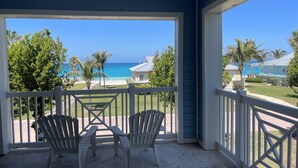 A covered porch with two Adirondack chairs, a ceiling fan, and a view of the ocean and beach. - Casa Azul welcomes you to a stunning ocean view condo steps away from the beach (Bailey Town)