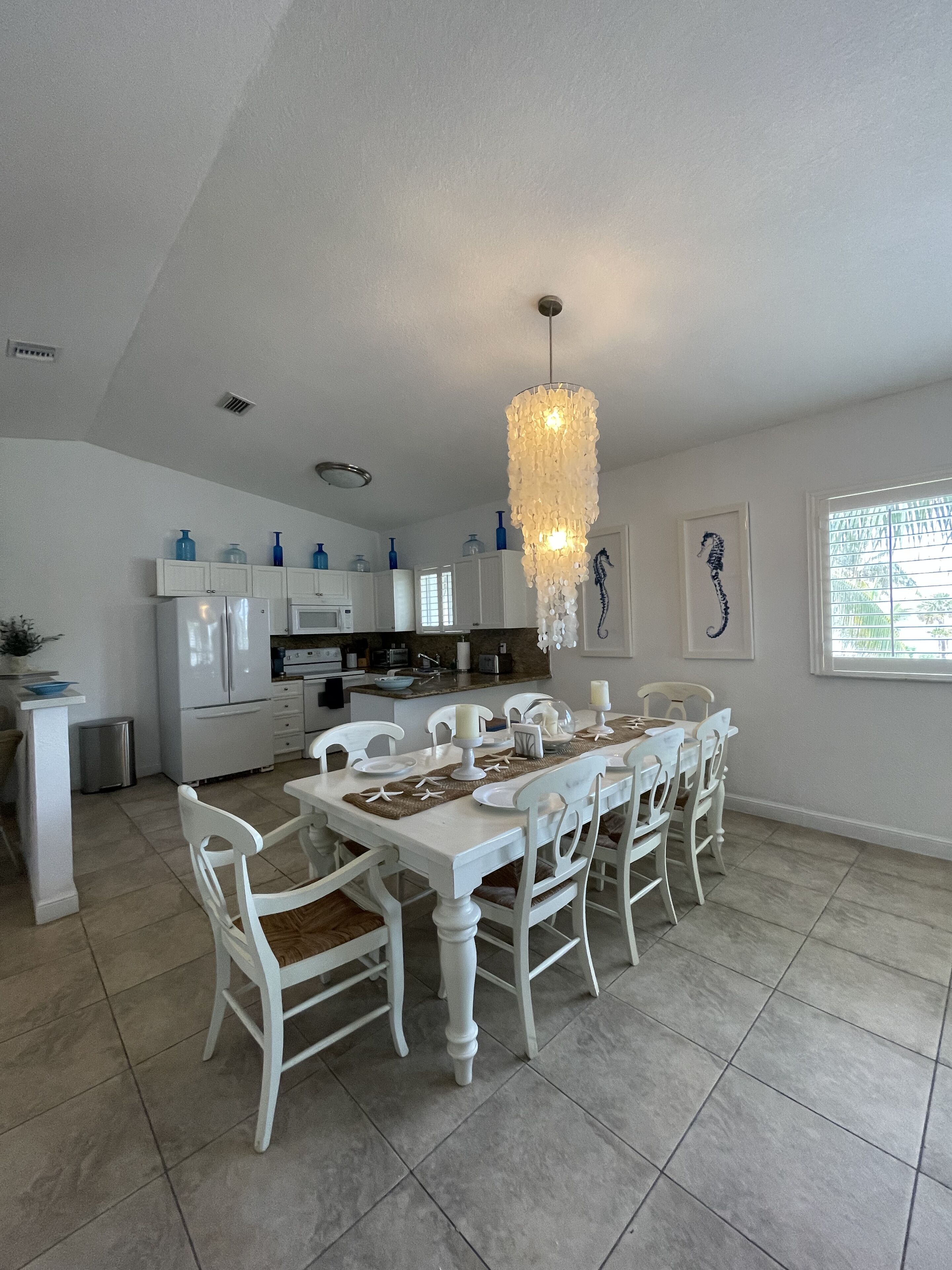 A spacious kitchen with white cabinetry, a dining area with white chairs, and a chandelier.