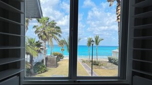 A room with a large window offering a view of a beach, palm trees, and a clear sky. - Casa Azul welcomes you to a stunning ocean view condo steps away from the beach (Bailey Town)