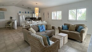 A spacious living area with a high ceiling fan, a kitchen in the background, and large windows allowing natural light. - Casa Azul welcomes you to a stunning ocean view condo steps away from the beach (Bailey Town)