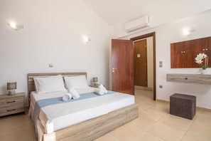 Une chambre à coucher comprenant un lit, des tables de chevet, un appareil de climatisation, une armoire en bois et un petit tabouret.