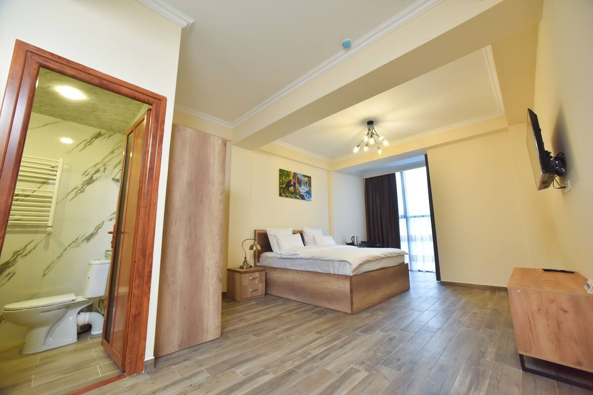 Un dormitorio con cama de madera, una mesita de noche, un espejo y un baño con inodoro y lavabo.