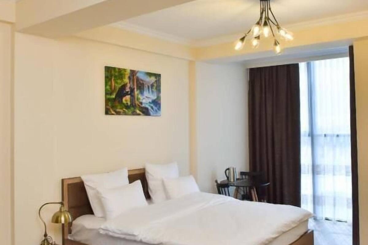 Una habitación de hotel con una cama grande, una mesita de noche, un escritorio y un cuadro en la pared.