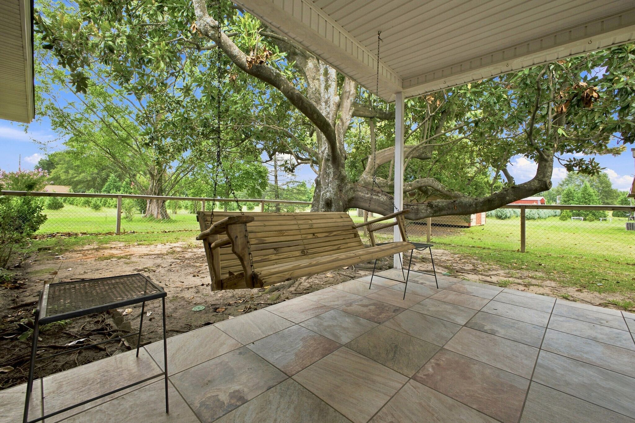 A covered patio with a swing, a metal table, and a tiled floor.