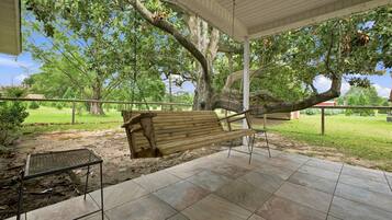 A covered patio with a swing, a metal table, and a tiled floor.