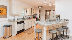 A modern kitchen with white cabinetry, granite countertops, and a central island with bar stools. - Historic FarmHouse with Goats & Glass Blowing (Hattiesburg)